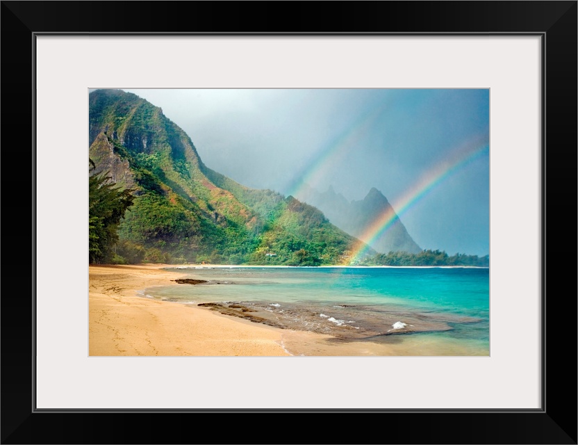 A landscape photograph with double rainbows on a tropical beach with mountains in the background.