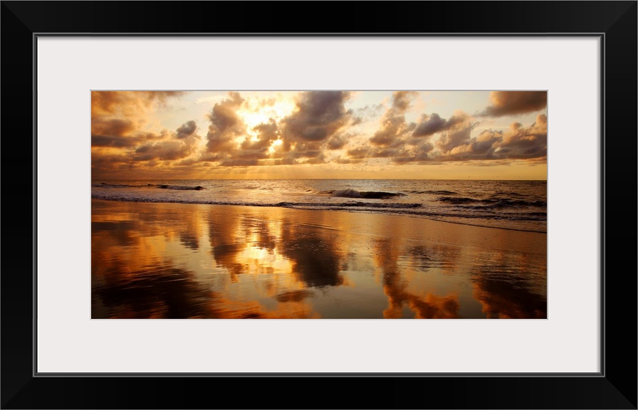 Panoramic photograph of seashore at dusk.  There is standing water on the beach and waves rolling in.  The dark cloudy sky...