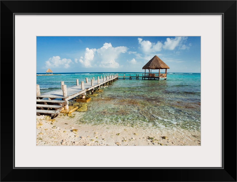 A pier stretches out into the clear ocean where there is a small hut sitting in the water.