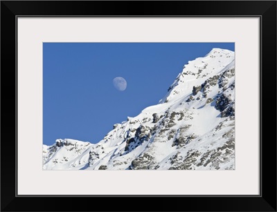 Moon rising over snow covered mountain peak at Hatcher Pass in Southcentral Alaska