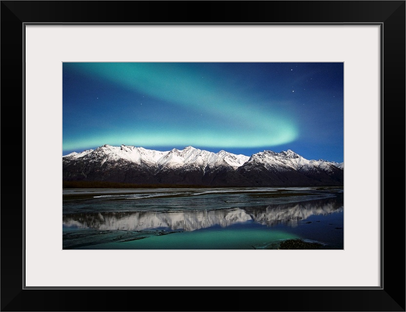 A landscape photograph of the aurora borealis and mountains reflecting in a lake filled with ice.