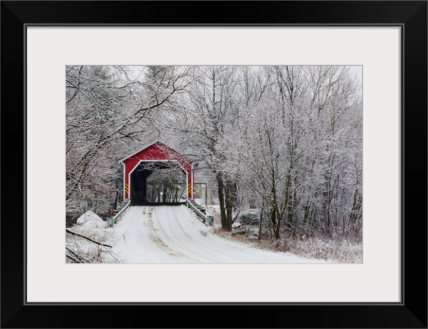 Snow covered trees surround a road that leads up to a covered bridge.