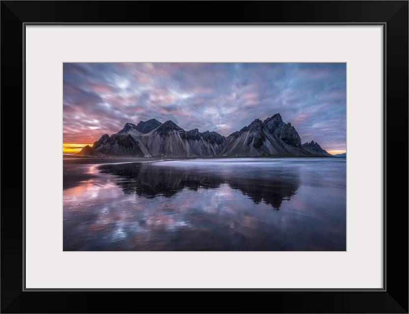 Rugged mountain peaks and a colourful sunset reflected in tranquil water. Iceland.