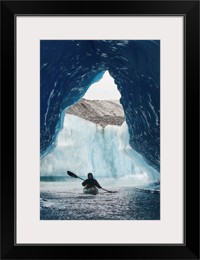 Sea Kayaker paddles through an ice cave amongst giant icebergs near Bear Glacier