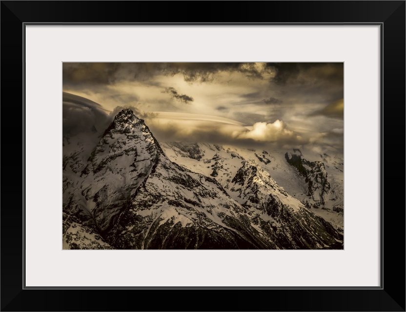 Dramatic view of snow-covered Caucasus mountains and glowing clouds, dombay region, Karachaevo-Cherkesskaya republic, Russia.