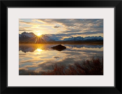 Sun rises over the Chugach Mountains with a pond and beaver lodge in the foreground