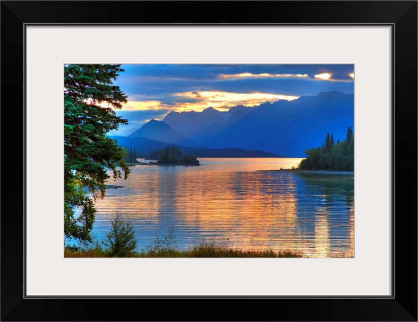 A landscape photograph of morning light reflecting on a lake in the mountains surrounded by trees.