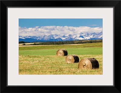 Three hay bales in a field with mountains, Alberta, Canada.