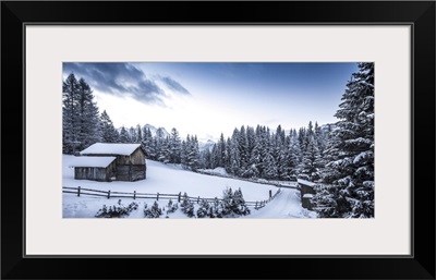 Winter Scene Looking Down At A Log Cabin Surrounded By Snow Covered Pine Trees, Italy