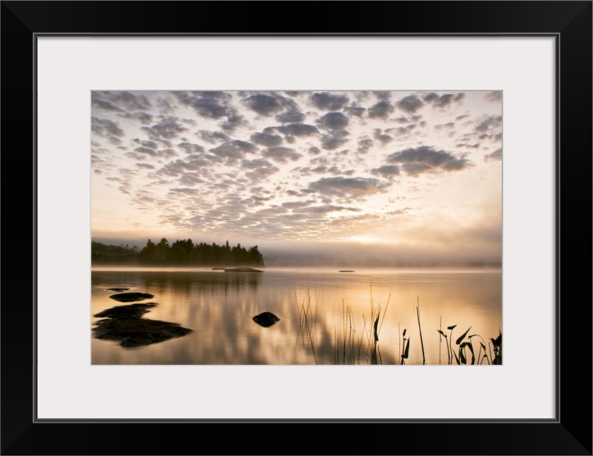 Horizontal photograph on a big wall hanging of the sun set reflecting in a large body of water, a distant tree line in the...