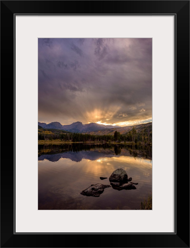 Landscape photograph of trees and mountains reflecting onto a calm lake at sunset.