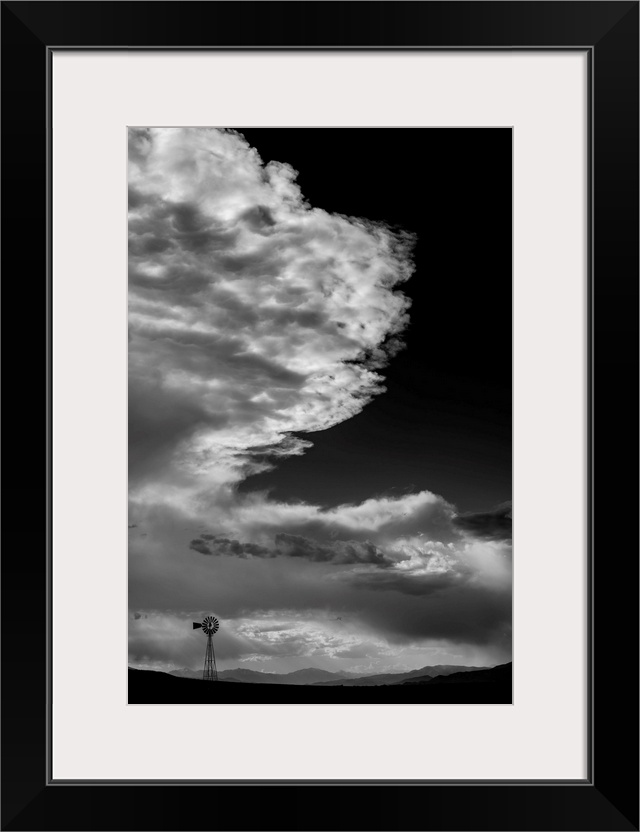 Black and white photograph of a beautiful cloudy sky with a windmill silhouette in the distance.