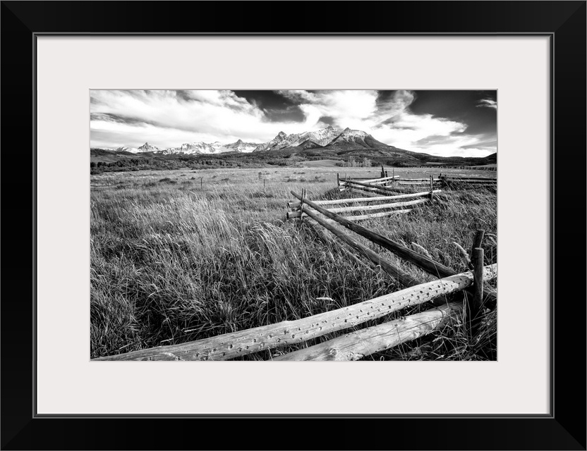 Black and white landscape photograph of a field with tall grass and a wooden fence creating leading lines to the mountain ...
