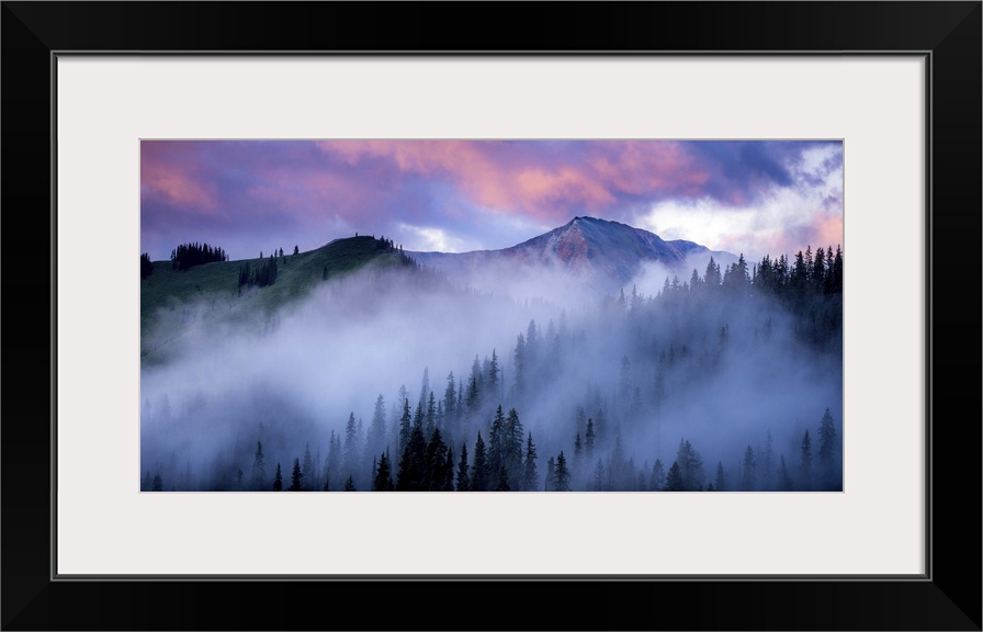 A photograph of mountain under dramatic clouds illuminated by the sunset.