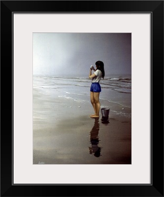 Girl Standing On Beach With Bucket By Her Feet, Looking At A Shell