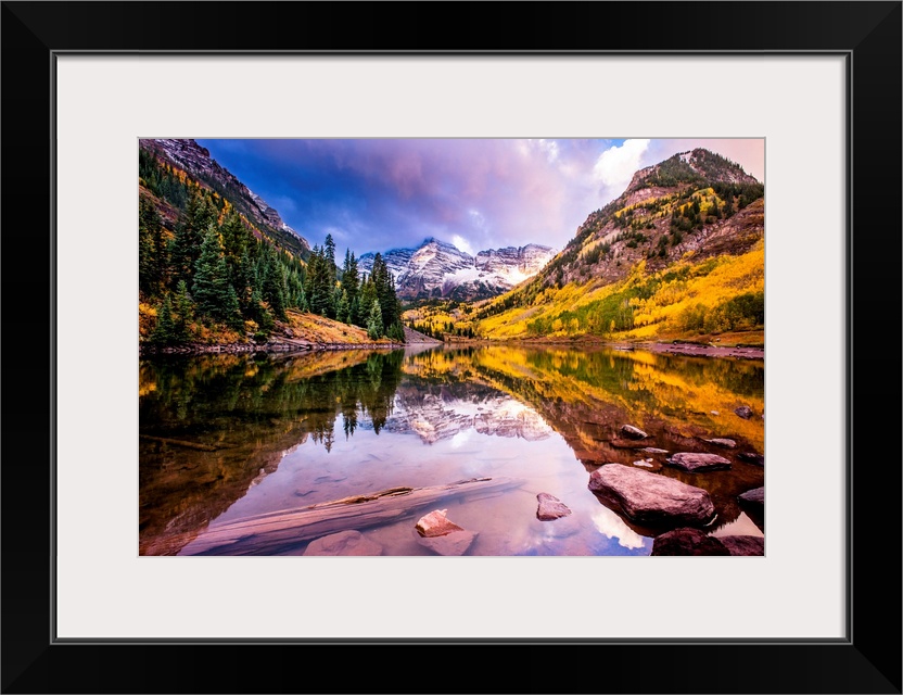 There is a warm hue to this photograph of mountainous terrain and thick foliage that reflect in still water below.