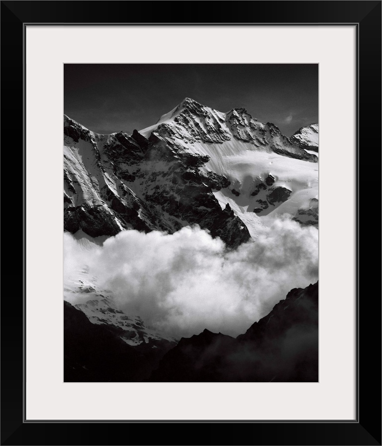 Black and white photograph of mountain peaks surrounded by rolling clouds.