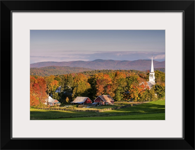 A photograph of the steeple of a white church sticking high up out of the autumn colored forest.