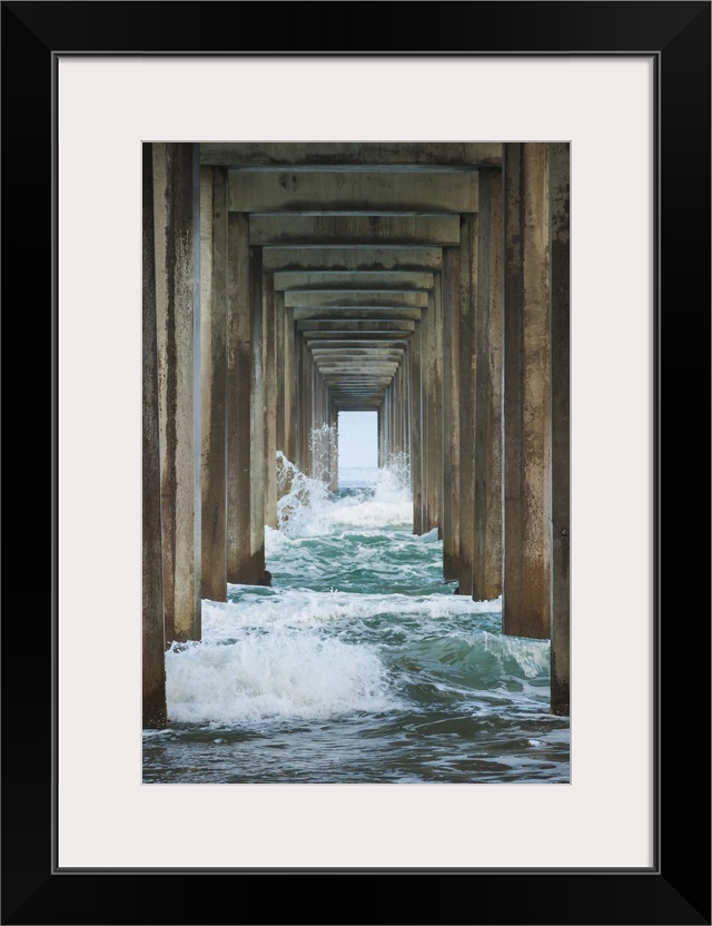 Photograph under a large pier looking out into the distance at the blue water.