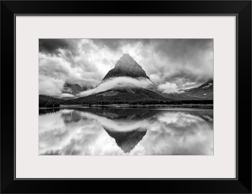 A black and white photograph of a pointed mountain surrounded by a ribbon of cloud while casting a perfect reflection in t...