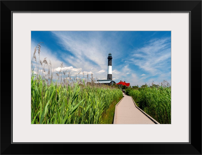 USA, New York, Long Island, wooden path to the Fire Island Lighthouse surrounded by beach grass, blue sky, white clouds.