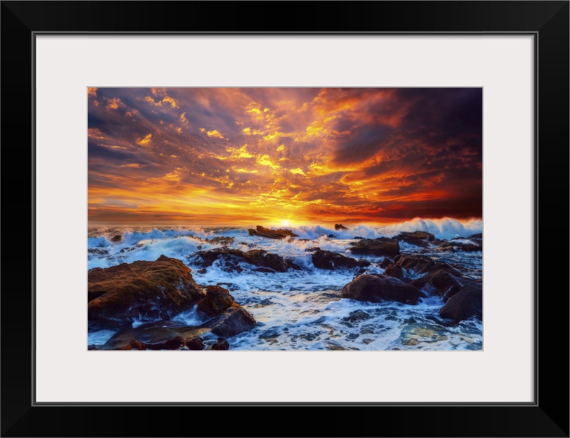 A bright fiery red sky illuminates crashing waves on the rocks in the ocean.