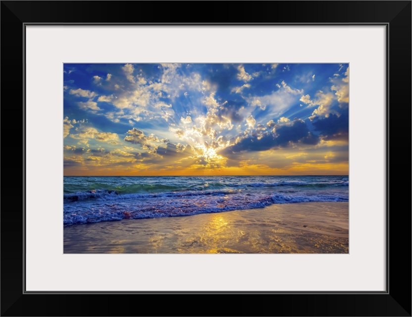 Sunrays at sunset break through the blue sky and cast golden sunlight onto the beach.