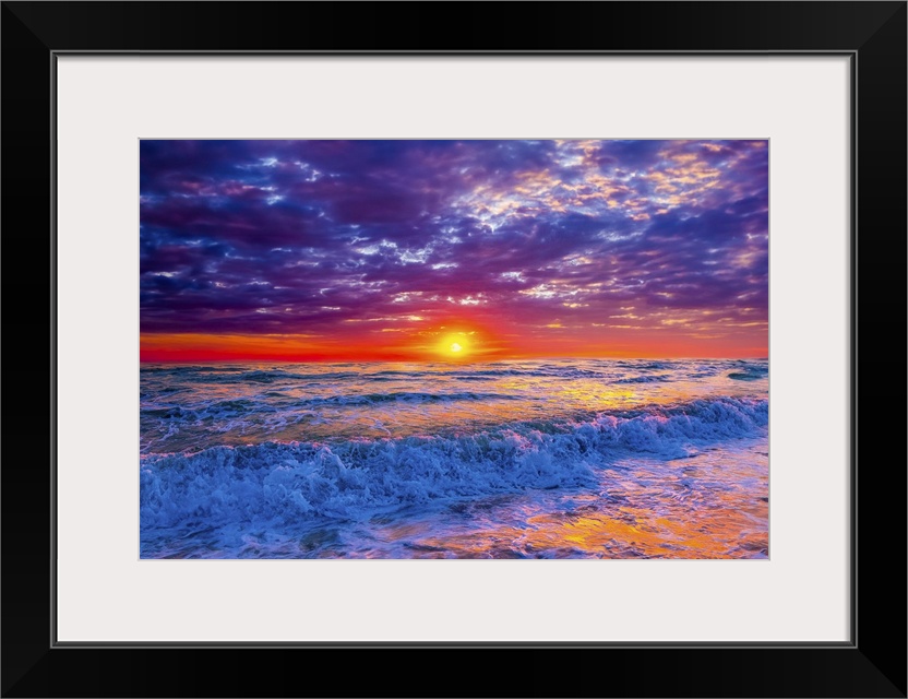 Blue ocean waves crash onto the beach beneath a red, lavender, and purple sunset.