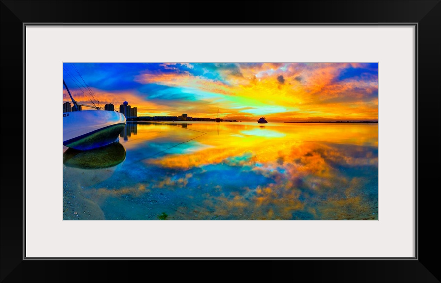A panoramic beach sunset with a burning bright reflection in the water. Yellow and blue sky reflecting in water and a boat...