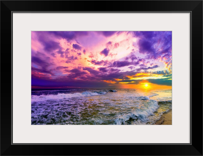 A beach sunset with beautiful pink and purple clouds. The ocean is littered with foamy waves under the pink sunset.