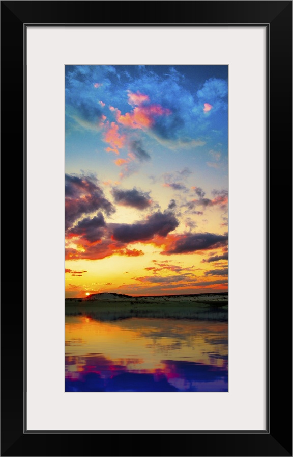 A tall vertical panorama of a sunset reflection on a lake with red and purple clouds.