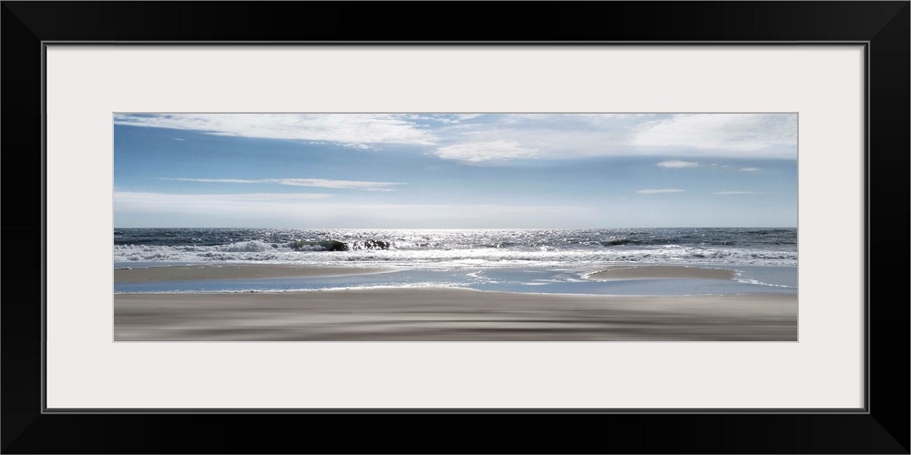A panoramic photo illustrating a tranquil view of the beach as the sun shimmers on the sea.