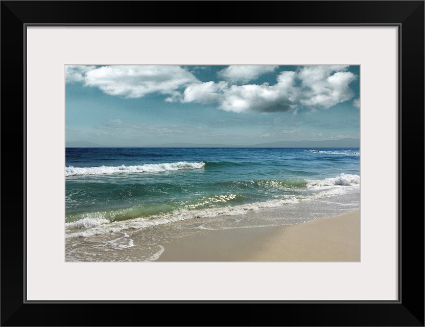 This serene photo shows rippling waves as they approach the beach with puffy white clouds in the background.