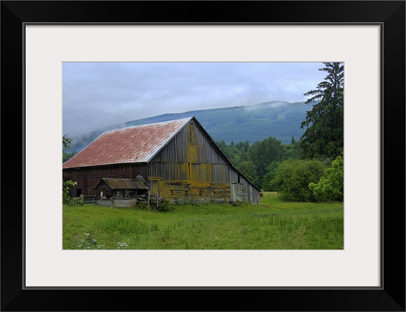 An old wooden barn in a rural field surrounded by fog.