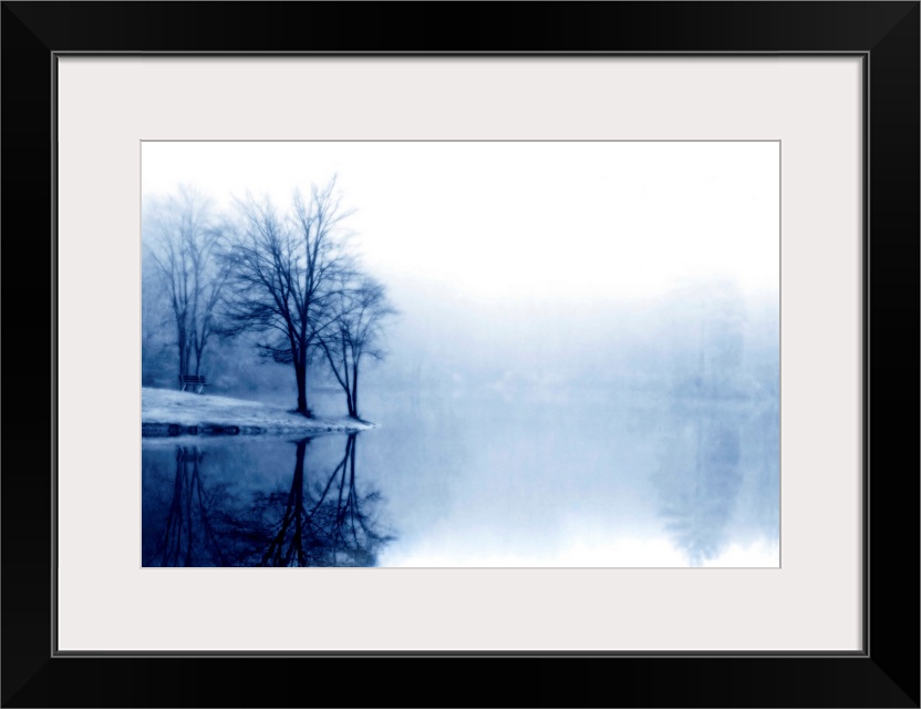 A photograph taken of a lake with bare trees off to the left side and more trees behind dense fog toward the back of the l...