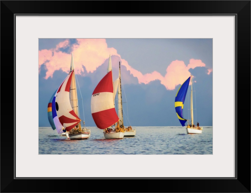 Sailboats with colorful sails on the water with large clouds in the sky.
