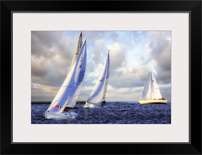 Several sail boats are pictured in open water and the sky filled with grey clouds.