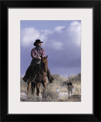 A cowboy poses on his horse with his dog