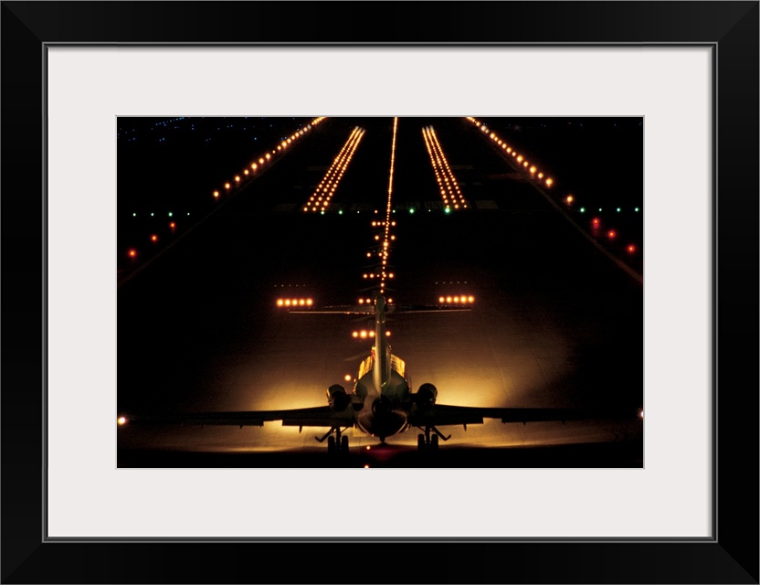 Giant photograph shows a small aircraft stationed at the end of a brightly lit airstrip at nighttime.