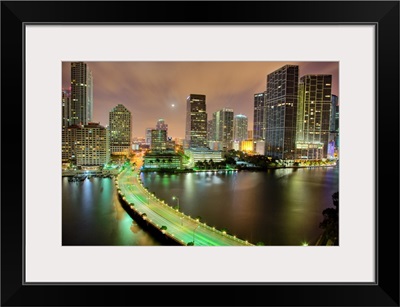 Bridge leads across waterway to downtown Miami sklyine at night.