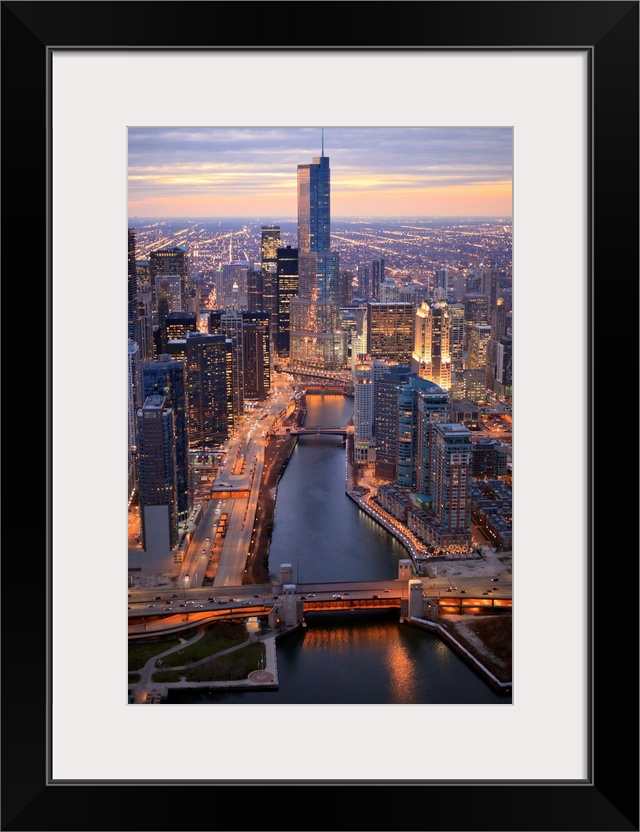 Vertical panoramic photograph of city skyline at dusk.  Building lights are shining and there is a river running through t...