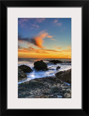 Dramatic sunset on rocky beach in Malibu, California.