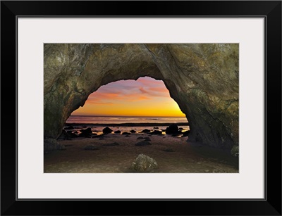 Dramatic sunset seen from inside cave on beach.