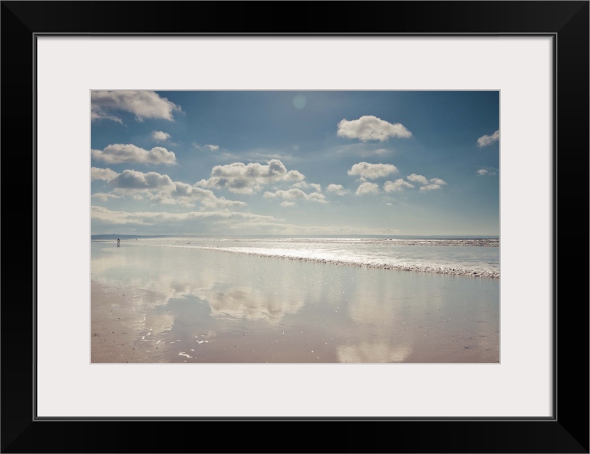 Empty beach with a thin film of water reflecting fluffy clouds in a sunny blue sky.