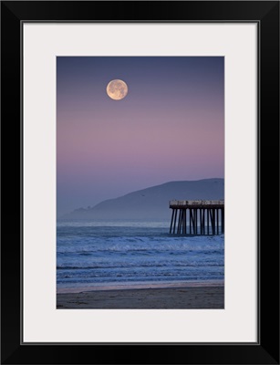 Full moon sets over  Pismo Beach at sunrise on winter morning.