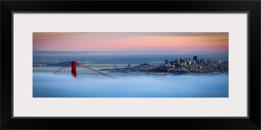 Panoramic photo of one of the tops of the Golden Gate bridge peeking through the dense fog with the cityscape seen in the ...