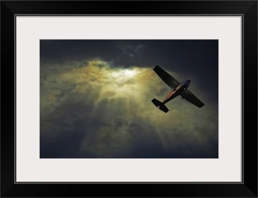 A photograph taken looking upward where rays of sunlight shine through dense cloud cover and a small airplane flies overhead.