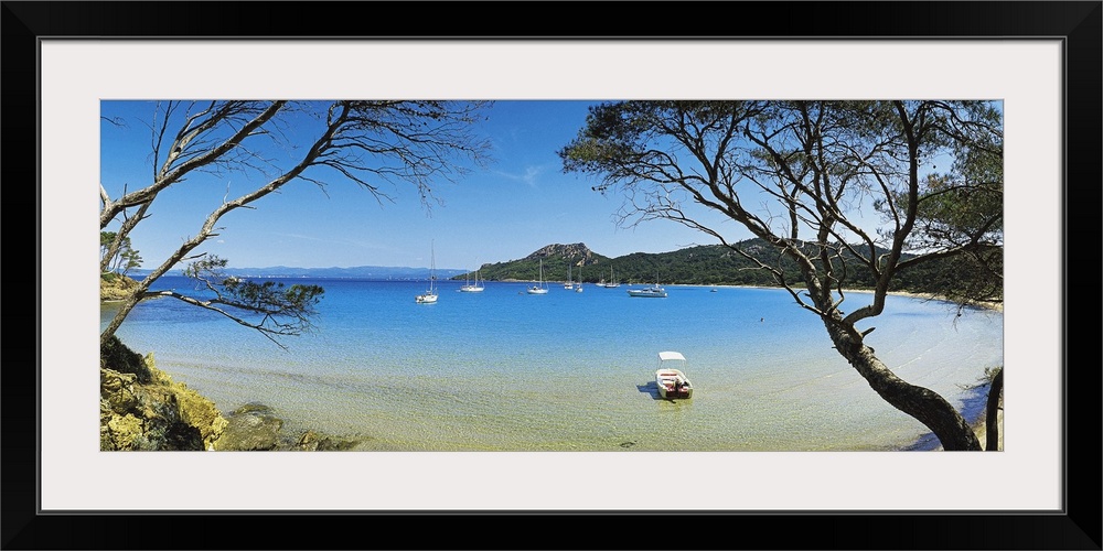 This panoramic shot was taken looking out at a lagoon with boats in the water and trees on both sides of the picture.