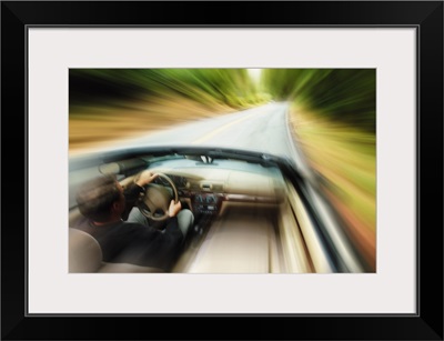 lifestyle photograph of a caucasian man driving fast down a road in a convertible