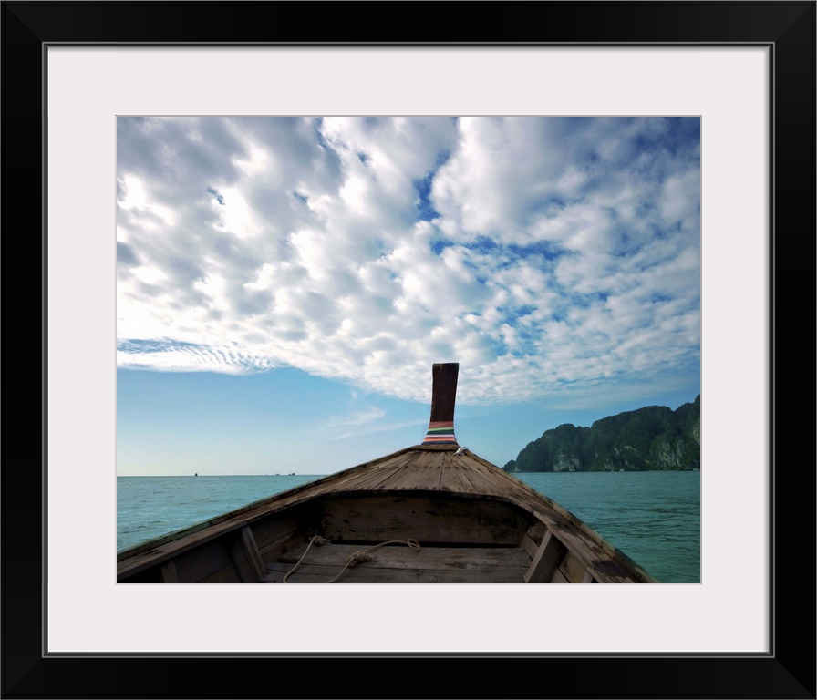 Long boat in sea with cloudy sky and mountain in background.